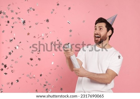 Emotional man blowing up party popper on pink background