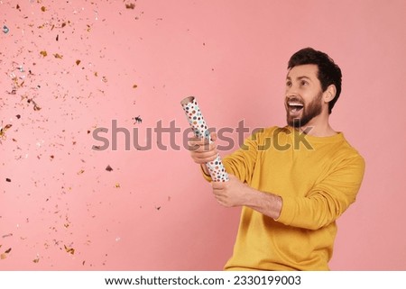Emotional man blowing up party popper on pink background. Space for text