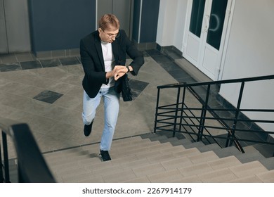 Emotional man checking time while walking up stairs in office. Being late