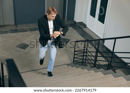 Emotional man checking time while walking up stairs in office. Being late