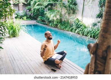 Emotional man freelancer raising hands celebrate achievement of successful online project and approved deal, overjoyed male with laptop computer feeling accomplished with digital nomad at pool terrace - Shutterstock ID 2147418953