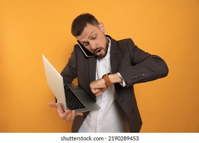 Emotional man with laptop checking time while talking on phone against orange background. Being late concept