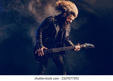 Emotional Man Rock Guitar Player With Long Hair And Beard Plays On The Black Background. Smoke Background. Studio Shot. 