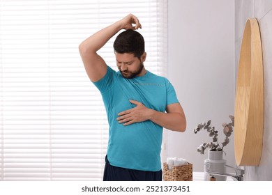 Emotional man in t-shirt before using deodorant at home