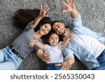 Emotional middle-eastern family father, mother and little daughter bonding on floor, cheerfully smiling and raising hands up, top view, closeup. Family, parenthood, parents and kids concept