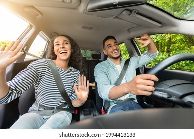 Emotional millennial mixed race couple handsome arab guy and pretty brunette lady having fun while car trip, listening to music and cherfully singing, shot from inside the auto, sun flare - Shutterstock ID 1994413133