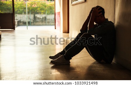 Emotional moment: man sitting holding head in hands, stressed sad young male having mental problems, feeling bad, depressed, disappointed, hopeless. Desperate man in dark corner needing care and help.
