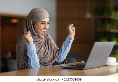 Emotional muslim woman in headscarf looking at laptop screen and raising hands up. Happy arab lady using laptop at cafe got good news, found nice job , empty space, career and job seeking concept - Powered by Shutterstock