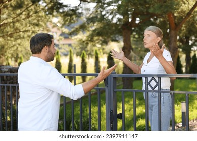 Emotional neighbours having argument near fence outdoors - Powered by Shutterstock