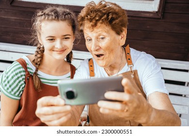 Emotional photo of grandmother and granddaughter using mobile phone for video call together getting good news, smiling and laughing. Carefree pensioner and teen girl chatting online on cell. - Powered by Shutterstock