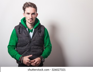 Emotional Portrait Of Attractive Young Man In A Grey Vest & Green Sweater With A Hood. Studio Photo. 