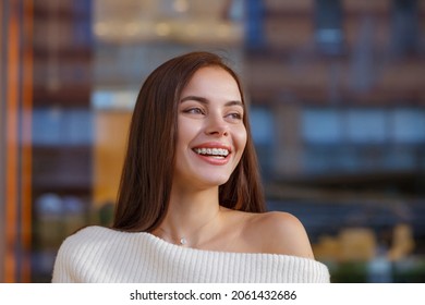 Emotional portrait of a beautiful happy smiling young woman with braces. Attractive girl bracket system posing in city outdoor. Brace, bracket, dental care, malocclusion, orthodontic health. Blurred