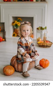 Emotional Portrait Of Cute Little Sad Astonished 1 Year Old Baby Toddler Kid Girl In Pumpkin Costume Sitting On Pumpkin Next To Fireplace At Home Smiling. Halloween Party Concept. Easy Costume Idea. 