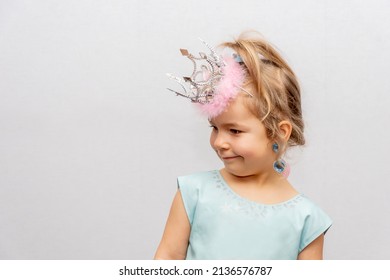 Emotional Portrait Of A Girl In A Crown And Earrings On A Light Background. Concept: A Little Princess, A Young Fashionista, Children's Jewelry For Girls.