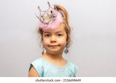 Emotional Portrait Of A Girl In A Crown And Earrings On A Light Background. Concept: A Little Princess, A Young Fashionista, Children's Jewelry For Girls.