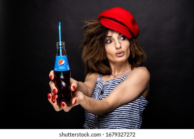 Emotional portrait of a girl in a red cap. Girl with a Pepsi bottle. Portrait on a black background.