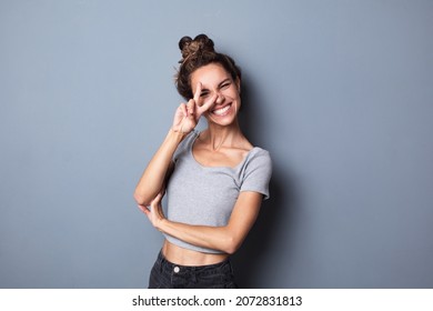 Emotional Portrait. Happy Excited Charming Woman Showing V-sign Isolated On Grey Color Background.