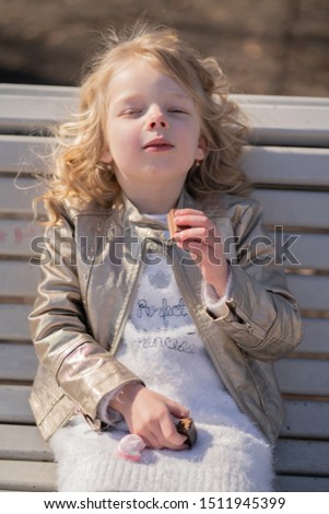 emotional portrait of a little girl with sweets, sitting on the bench in the city park outdoor alone. pretty child have a bad tasty snack.