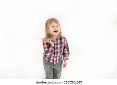 Emotional portrait of a naughty and positive little blond girl in a checkered shirt looking with a laugh at the screen holding a smartphone isolated on a white background. Happy childhood. Positive - Powered by Shutterstock