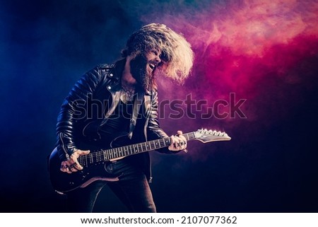 Emotional portrait of a rock guitar player with long hair and beard plays on the black background. Smoke background. Studio shot. 