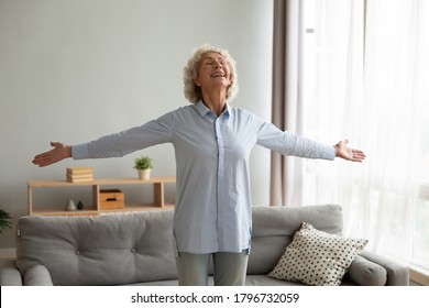 Emotional Positive Middle Aged Senior Retired Woman Standing With Outstretched Arms, Celebrating Freedom Alone At Home. Overjoyed Mature Old Female Retiree Dancing Indoors, Feeling Excited Optimistic.