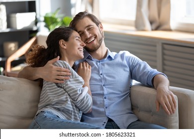 Emotional positive romantic family couple laughing at funny joke, relaxing together on sofa indoors. Happy young pretty woman enjoying communicating with beloved man at home dating, relations concept. - Shutterstock ID 1805623321