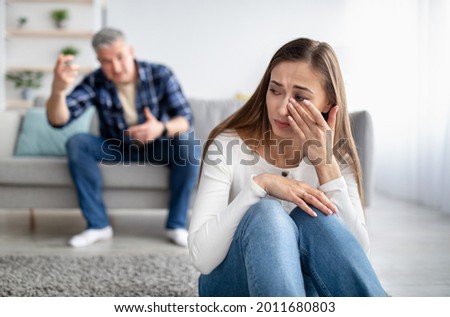 Emotional or psychological domestic violence concept. Mature man abusing his depressed wife, shouting, humiliating and threatening her, middle aged woman crying on floor at home
