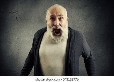 emotional screaming senior man with beard over dark wall