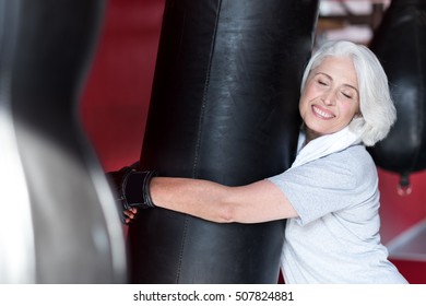 Emotional Smiling Senior Woman Hugging Punching Bag.