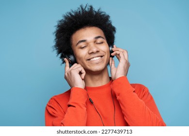 Emotional stylish African American man wearing headphones listening music, singing song and enjoying isolated on blue background  - Powered by Shutterstock