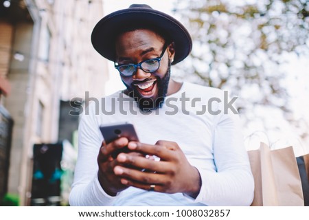 Emotional surprised african american guy with low prices in web store receiving message with promo code,excited dark skinned hipster guy in trendy hat overjoyed with winning online contest on web site