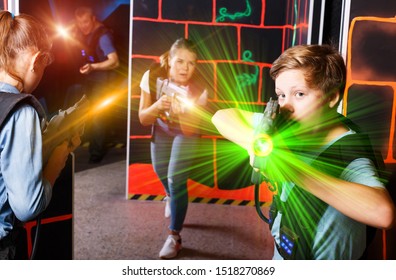 Emotional teen boy with laser pistol playing laser tag with his family on dark labyrinth