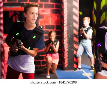 Emotional teen boy with laser pistol playing laser tag with friends on dark labyrinth..