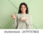 Emotional woman eating tasty cereal rings against color wall