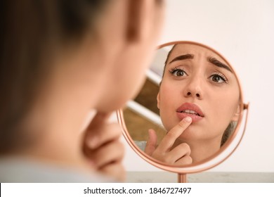 Emotional woman with herpes touching lips in front of mirror against light background - Shutterstock ID 1846727497