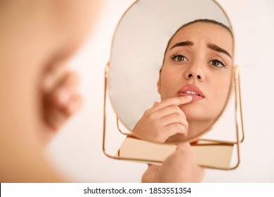 Emotional woman with herpes touching lips in front of mirror against light background - Shutterstock ID 1853551354