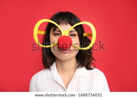 Emotional woman with large glasses and clown nose on red background. April fool's day