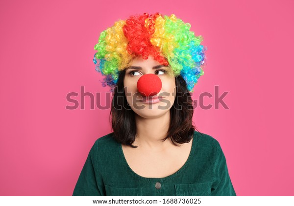 Emotional woman with rainbow wig and clown\
nose on pink background. April fool\'s\
day