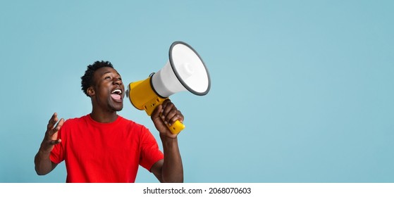 Emotional Young Black Guy Making Announcement With Megaphone In Hands, Cheerful African American Man Using Loudspeaker For Sharing News While Standing Over Blue Background, Panorama With Copy Space