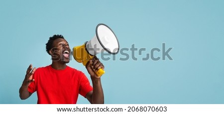 Emotional Young Black Guy Making Announcement With Megaphone In Hands, Cheerful African American Man Using Loudspeaker For Sharing News While Standing Over Blue Background, Panorama With Copy Space