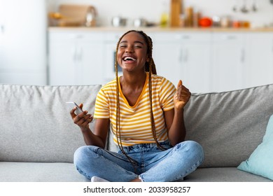 Emotional Young Black Woman Gambling Or Trading On Stocks Online, Buying Cryptocurrency, Using Modern Smartphone, Afro American Millennial Lady Sitting On Couch, Celebrating Success, Copy Space