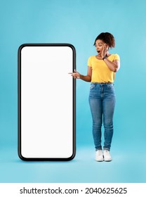 Emotional young black woman pointing at empty smartphone in shock on blue studio background, mockup for your website or mobile app design. Cellphone screen template - Shutterstock ID 2040625625