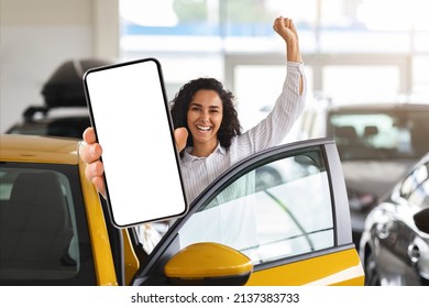 Emotional Young Brunette Woman Choosing New Car, Standing By Brand New Yellow Auto, Showing Modern Cell Phone With White Blank Screen And Raissing Hand Up, Using Auto Dealership App, Mockup