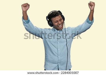 Emotional young Indian man wears blue shirt listen to music in headphones. Isolated on white background.