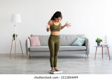 Emotional young Indian woman standing on scales, feeling disappointed about her weight loss, failing to achieve slimming result at home, copy space. Unsuccessful dieting concept