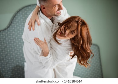 Emotional young lady opening her mouth and laughing with closed eyes while loving man holding her in his arms and hugging - Shutterstock ID 1418184614