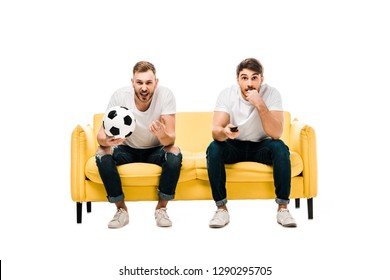 Emotional Young Men With Soccer Ball Sitting On Couch And Watching Sports Match Isolated On White