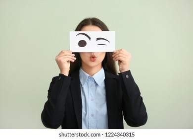 Emotional Young Woman Hiding Face Behind Sheet Of Paper With Drawn Eyes On Light Background