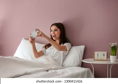 Emotional Young Woman Playing Mobile Game In Bed At Home