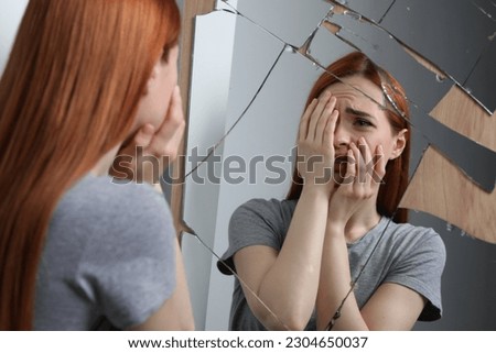 Emotional young woman suffering from mental problems near broken mirror